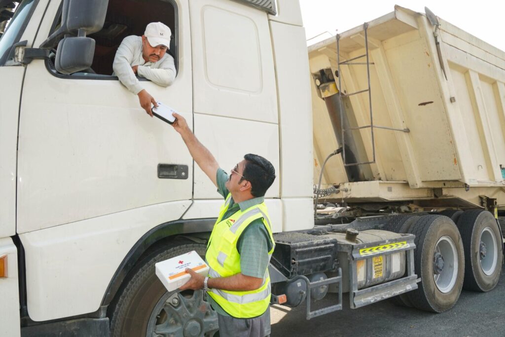 RTA and Dubai Police officers inspecting heavy vehicle tyres and distributing multi-lingual safety manuals to truck drivers at a highway rest area.