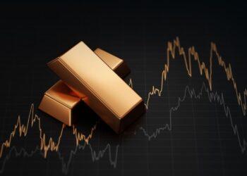 Stack of gold bullion bars and financial market trading screen display